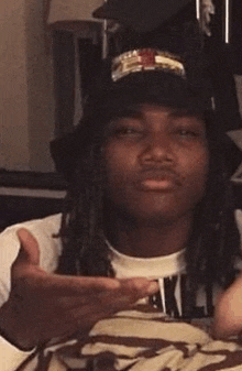 a man with dreadlocks is wearing a hat and a t-shirt .