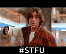 a man in a plaid shirt is pointing his fist at the camera with the hashtag #stfu .