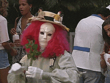 a woman with pink hair is wearing a white mask and holding a rose