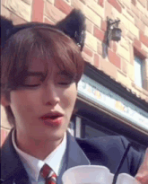 a man wearing a cat ear headband and a tie is holding a cup of coffee .