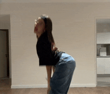 a woman in a black shirt and jeans is dancing in a room