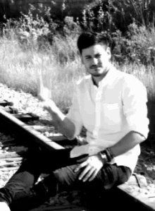 a man in a white shirt sits on train tracks