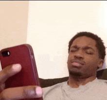 a man is sitting on a bed looking at his cell phone .