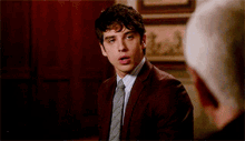a man in a suit and tie is talking to another man in a room