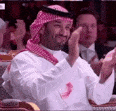 a man in a keffiyeh is applauding while sitting in a chair .