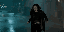 a woman in a black jacket is walking down a wet street at night