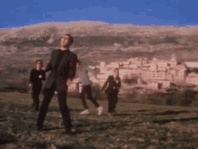 a group of people are dancing in a field in front of a mountain and a small town .