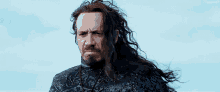 a man with long hair and a beard is standing in the wind