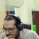 a man wearing headphones and glasses is sitting in a chair with his hand on his chin