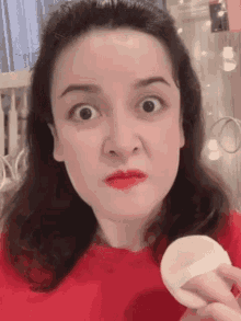 a woman in a red shirt is making a funny face while holding a sponge in her hand .