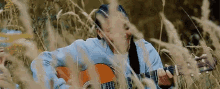 a woman is playing a guitar in the tall grass .