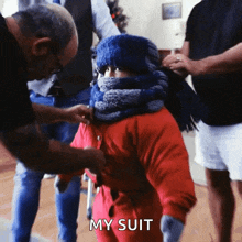 a child wearing a red jacket and scarf is being helped by a man who says my suit