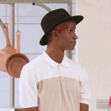 a man wearing a hat and a polo shirt is standing in front of pots hanging on a rack