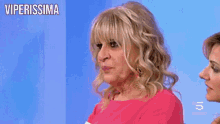 a woman in a pink shirt is standing in front of a blue wall with the words viperissima on it