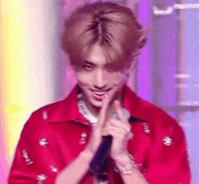 a young man in a red shirt is holding a microphone and making a heart shape with his hands .