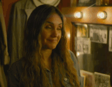 a woman is smiling in front of a mirror with a picture of a man on the wall behind her
