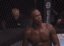 a shirtless man sits in front of a fence that says the sniper