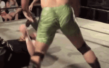 a man in green shorts is wrestling another man in black shorts .