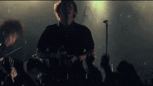 a man singing into a microphone in front of a crowd with the letter d in the corner