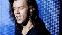 a man with long hair is standing in front of a blue screen .