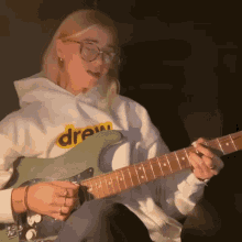 a woman wearing a drew sweatshirt is playing a guitar