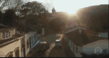 a car is driving down a narrow street with the sun shining through the roofs