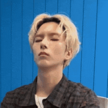 a young man with blonde hair is sitting in front of a blue wall .