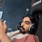 a man with a beard is sitting in a chair wearing headphones and looking at a cell phone .