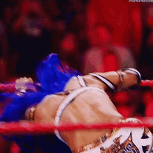 a female wrestler with blue hair is laying in a wrestling ring .