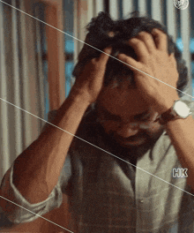 a man wearing glasses is holding his head with his hands .