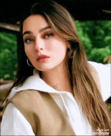 a woman with long hair and earrings is wearing a white shirt and a tan vest .