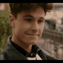 a young man wearing a black leather jacket and a black shirt is smiling .