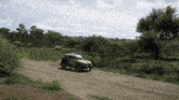 a car is driving down a dirt road with trees in the background