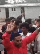 a man in a red shirt is dancing in front of a crowd of people with his arms in the air .