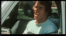 a man is sitting in the driver 's seat of a car laughing .