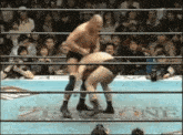two men are wrestling in a ring with a crowd watching and the word one is on the wall behind them .