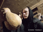 a man in a black hoodie is holding a large pumpkin in his hands