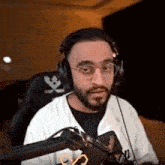 a man with a beard and glasses is wearing headphones and sitting in front of a microphone .