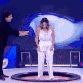 a woman in white pants is standing in a circle on a stage with a man in a black suit behind her .
