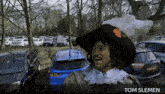a man in a hat is standing in a parking lot and the name tom slemen is on the bottom right
