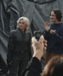 a man is taking a picture of a woman in a black suit and a man in a blue sweater .