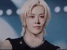 a close up of a man with blonde hair wearing a black shirt and a necklace