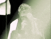 a man with glasses singing into a microphone in a green light