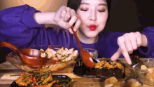a woman in a purple sweater is eating food with a spoon