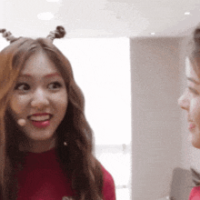 a woman wearing a red sweater and a microphone looks at another woman