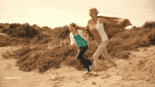 a woman and a child are running on a sand dune with the number 156611115