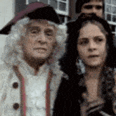 a man in a wig is standing next to a woman in a black hat .