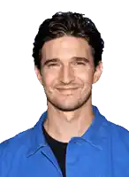 a man wearing a blue shirt with a black shirt underneath is smiling