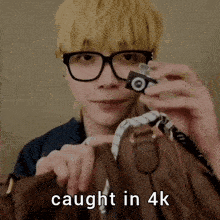 a man wearing glasses is holding a small camera over a brown purse with the words caught in 4k below him