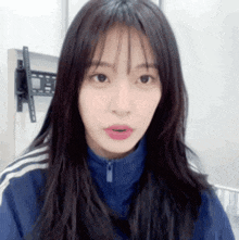 a woman with long hair and bangs is wearing a blue jacket and looking at the camera .